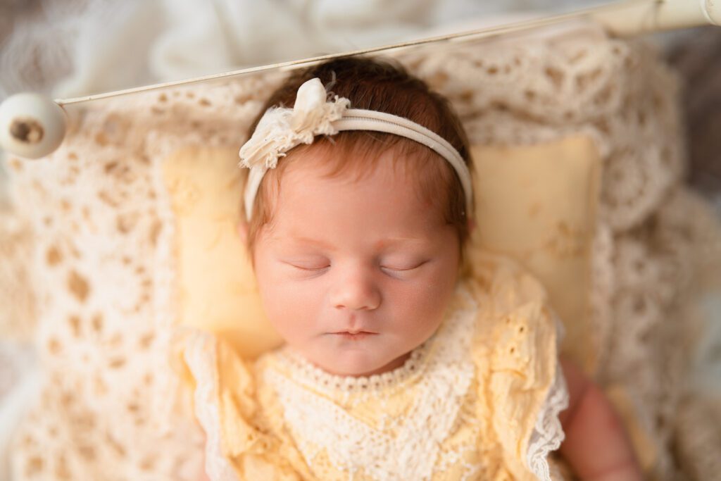 Sleeping newborn baby girl with red hair wearing a yellow lace outfit and matching bow headband.