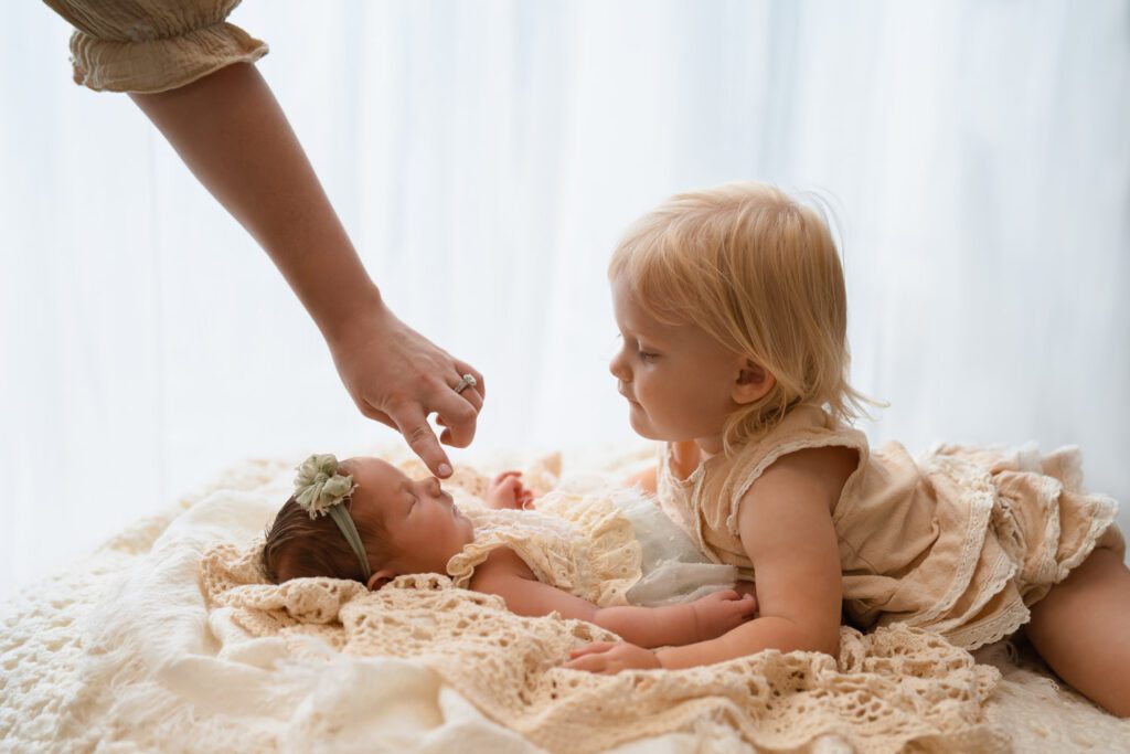 big sister looking down as mom gently touches the newborn’s nose.