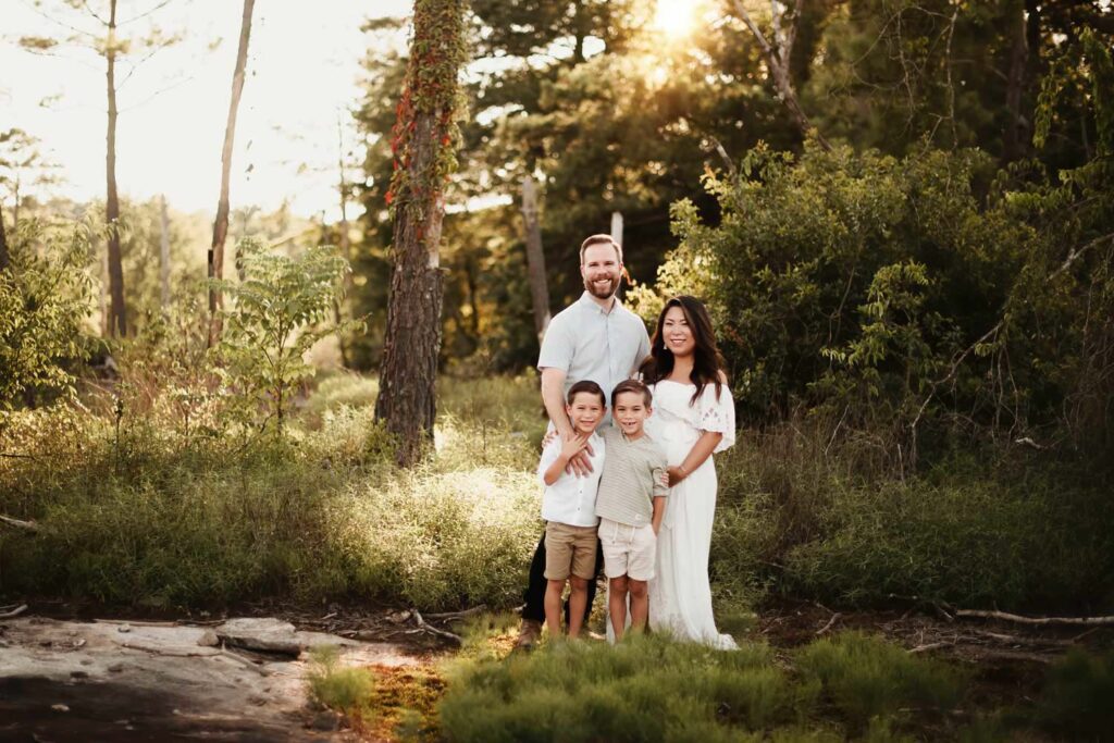 family of four standing together surrounded by trees at sunset during an Arabia Mountain maternity session.