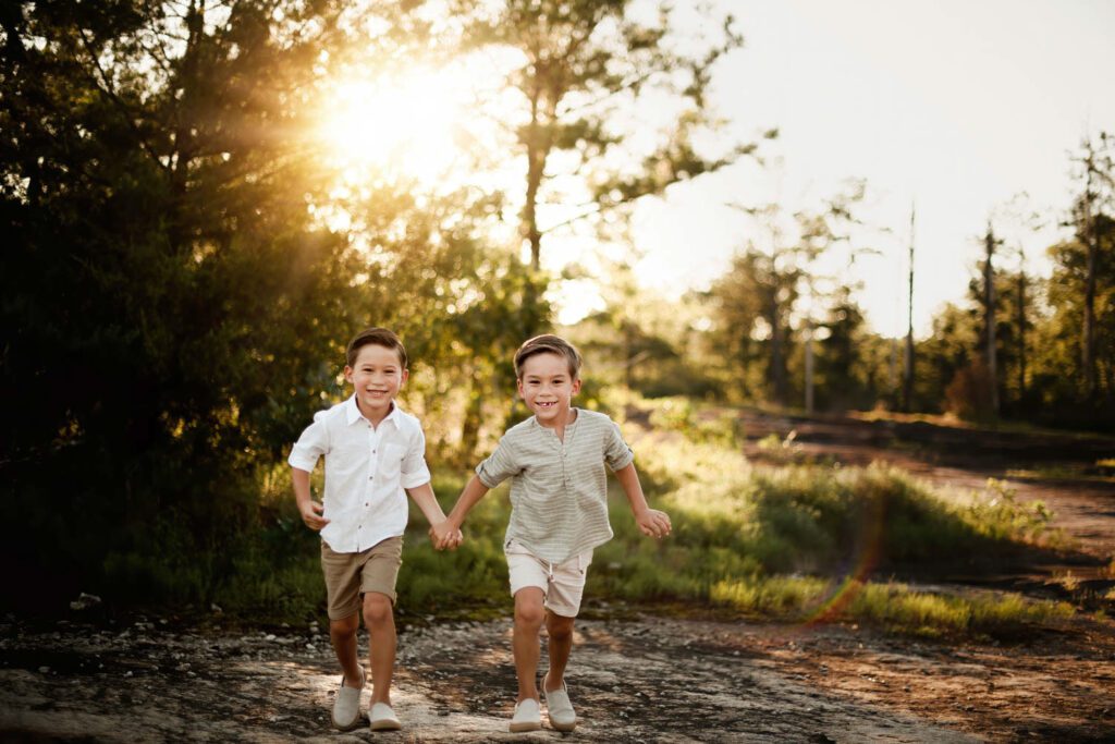 twin brothers holding hands and running towards camera in the forest at Arabia Mountain at sunset.