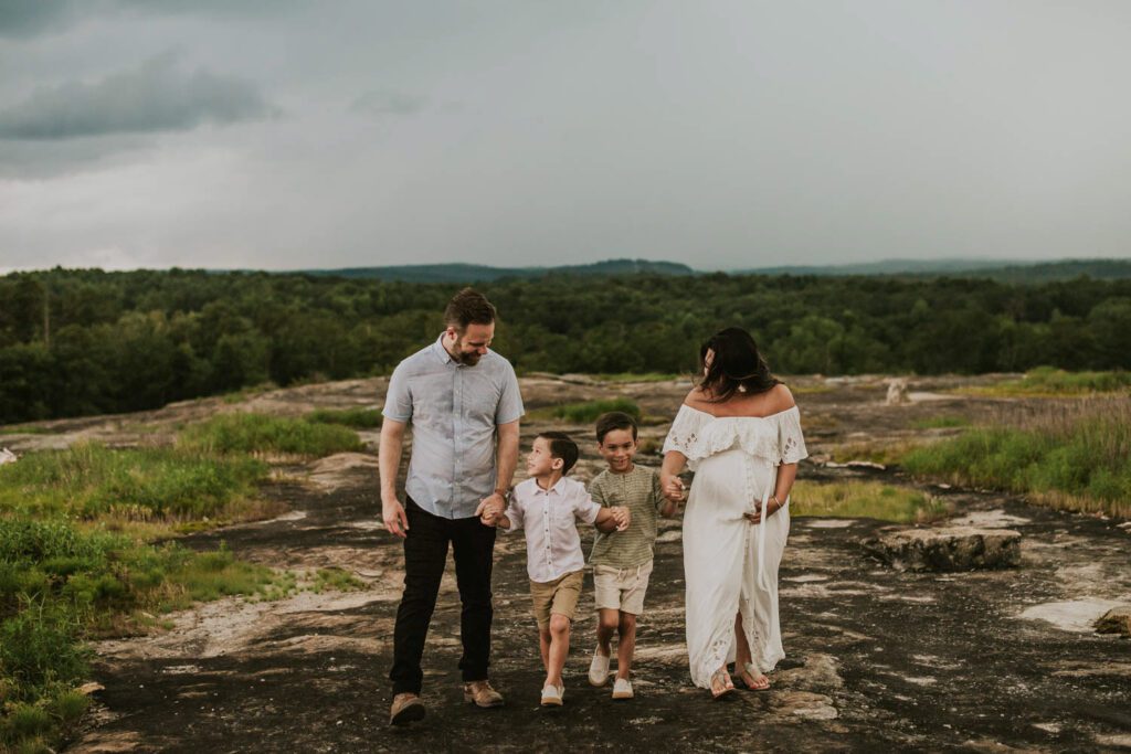 expecting mom walking hand in hand with her family across riverbed after a storm during maternity photos session