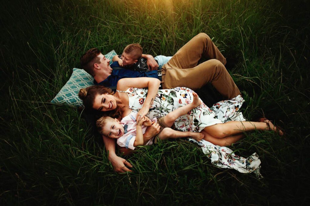 Mom in a colorful white floral dress while one son wears a pink shirt with a bowtie and her other boys wear darker shirts. 