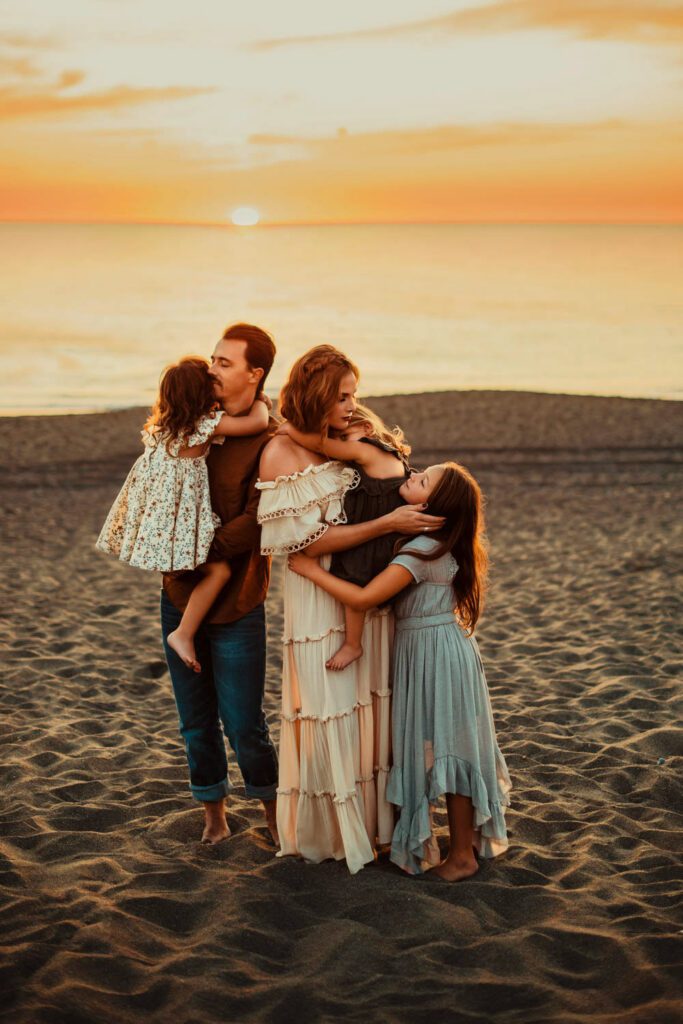 Mom in a cream gown, eldest daughter in a grey ruffled dress, younger girls in green and floral dresses with dad in jeans. 